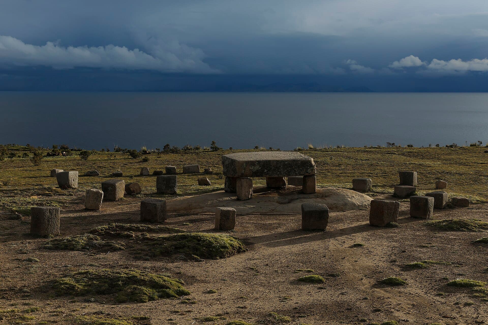 A stone altar set toward Lake Titicaca under a storm-lit sky