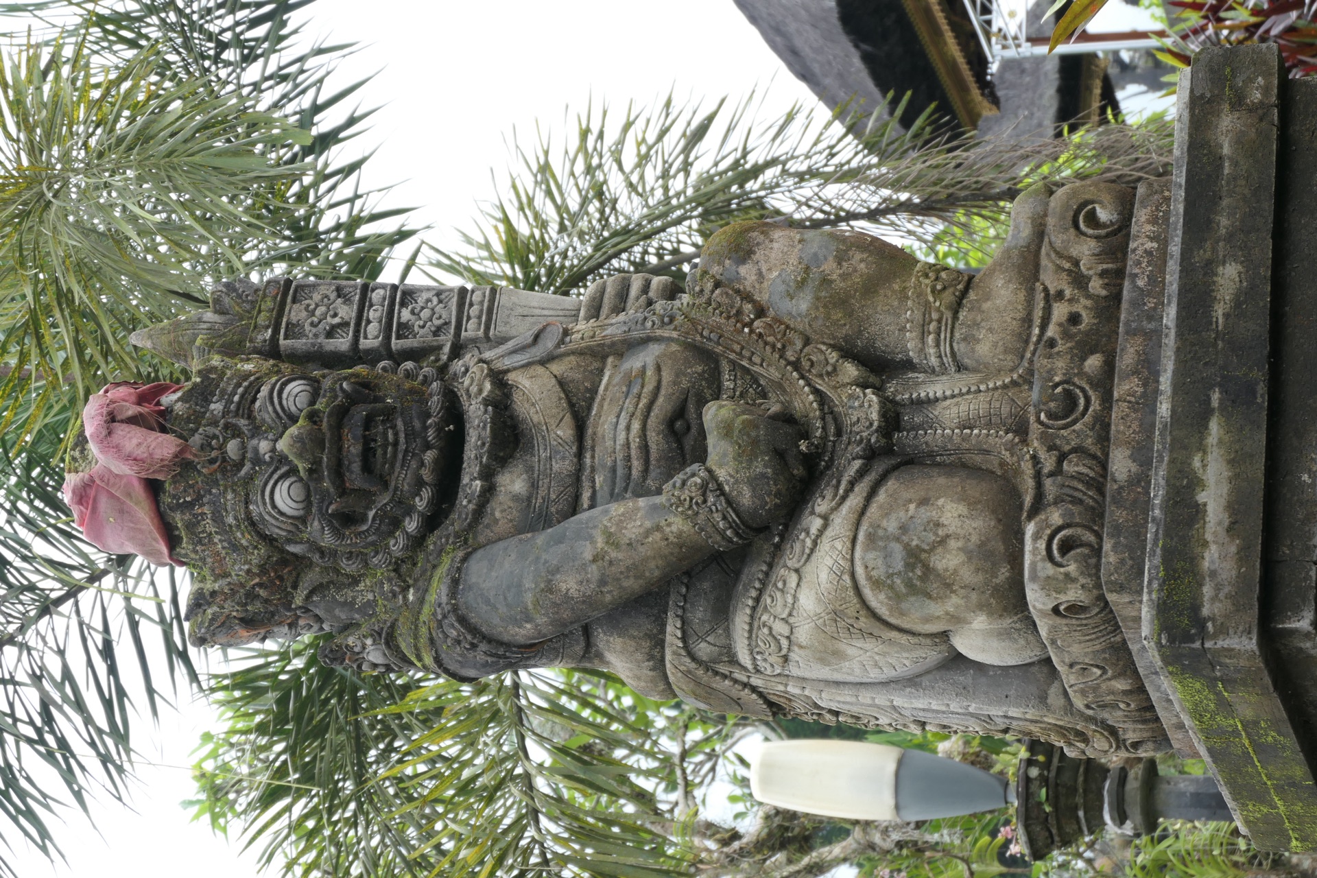 A dvarapala guardian statue of Besakih, a red frangipani offering on its head