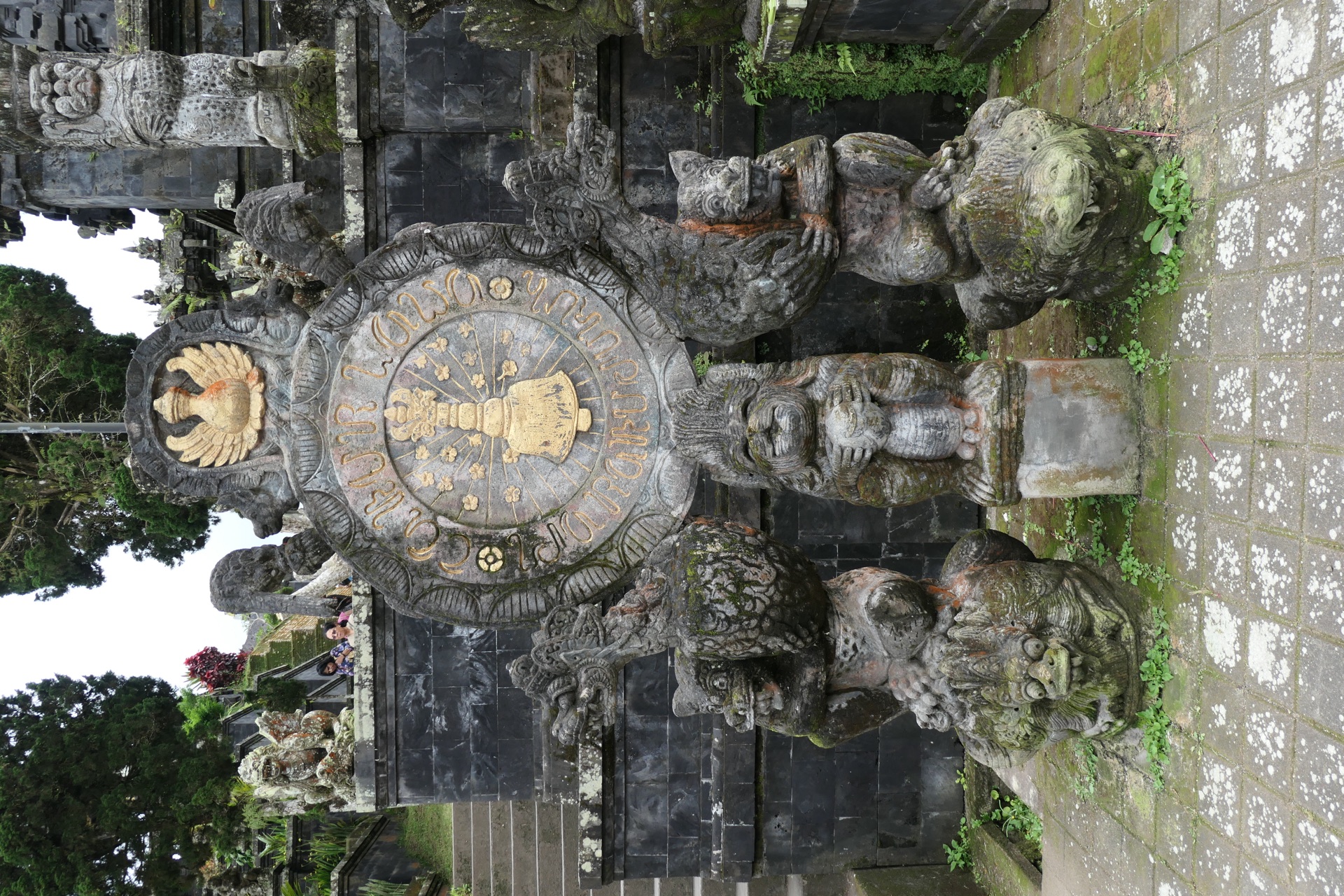 A golden disc mounted on a black stone shrine, small deity figures below
