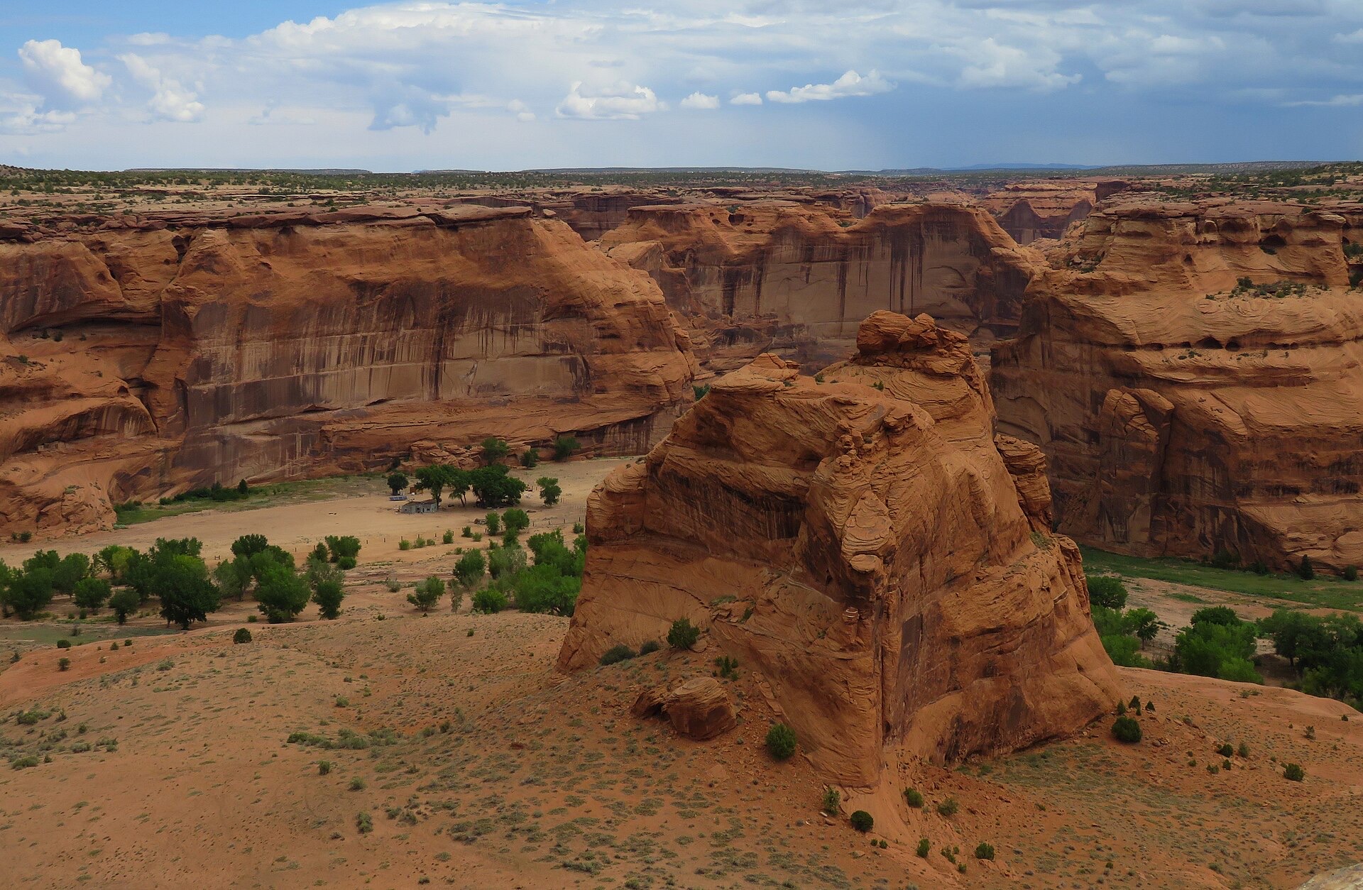 Green fields and trees among the red cliffs, a canyon home beside them