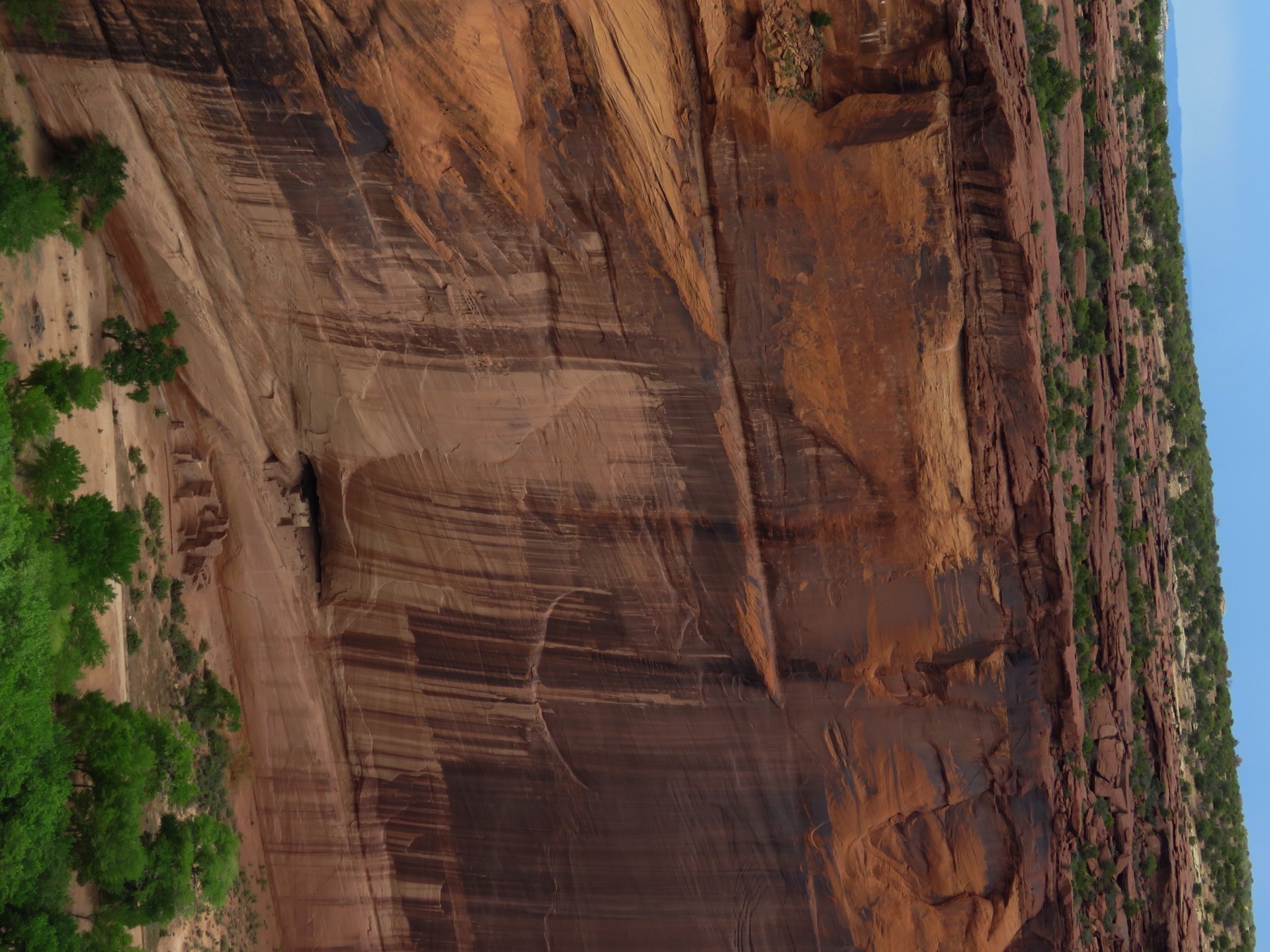 The White House Ruin nestled beneath a towering red cliff streaked with dark desert varnish