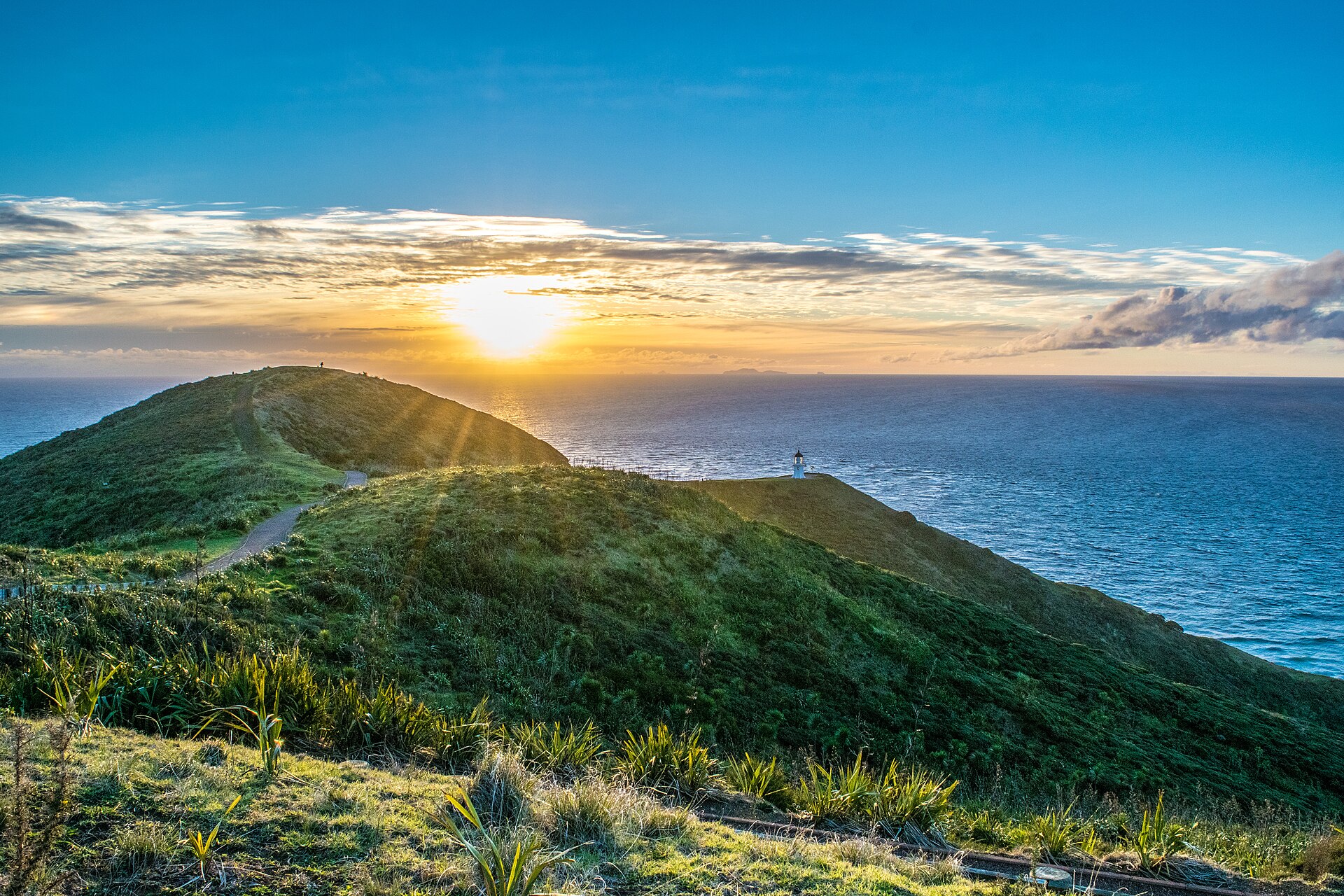 The sun setting over the sea beyond the small lighthouse at the cape's tip