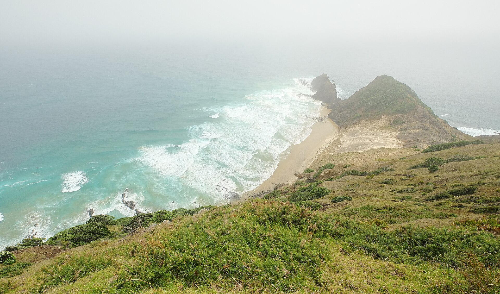 The cape of Cape Reinga wrapped in low fog and white surf