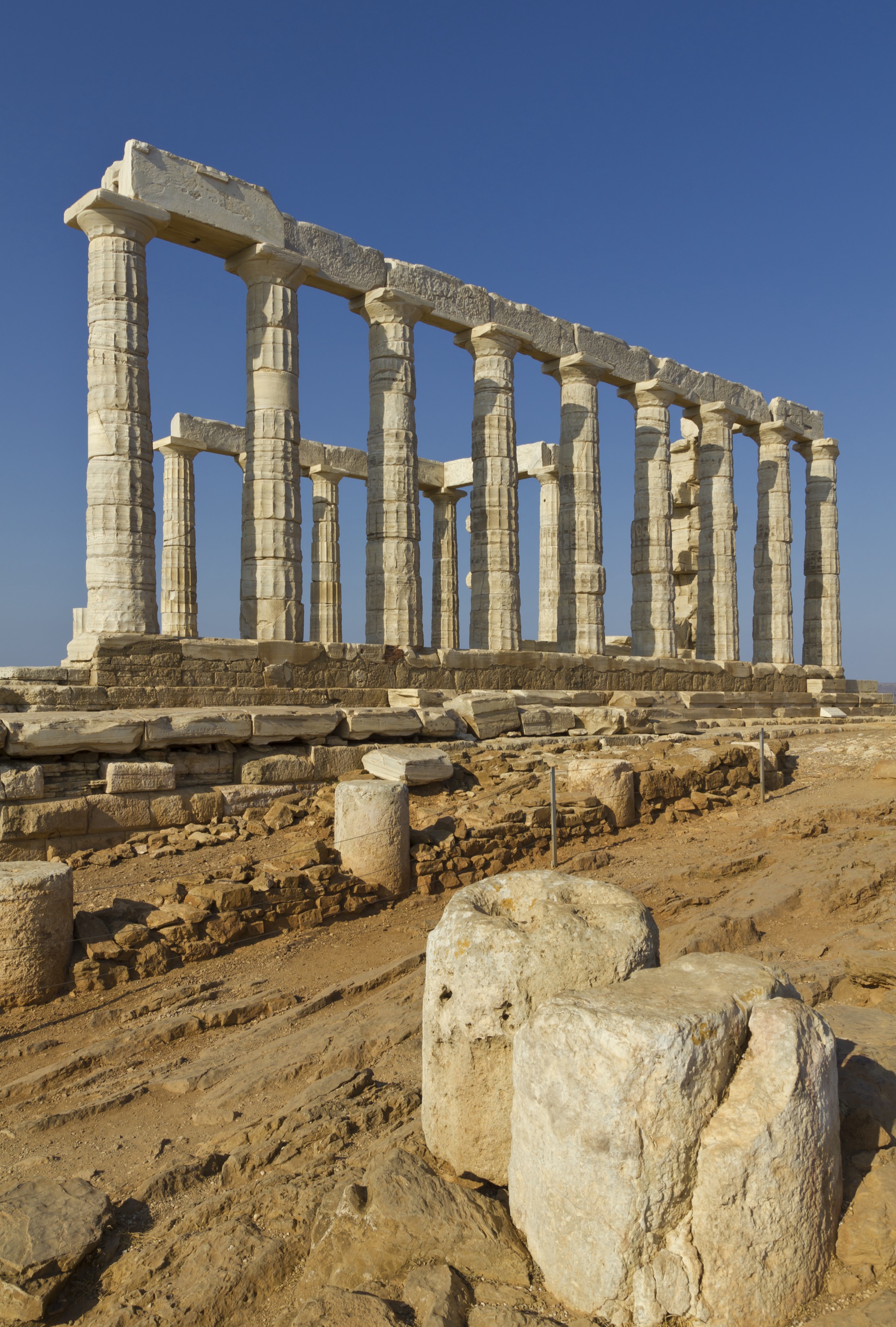 The Doric colonnade of the Temple of Poseidon in warm afternoon light, fallen column drums at its foot