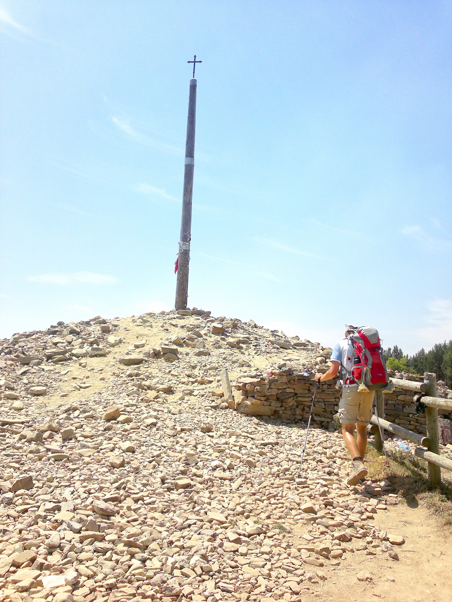 A pilgrim climbing the mound of stones toward the iron cross