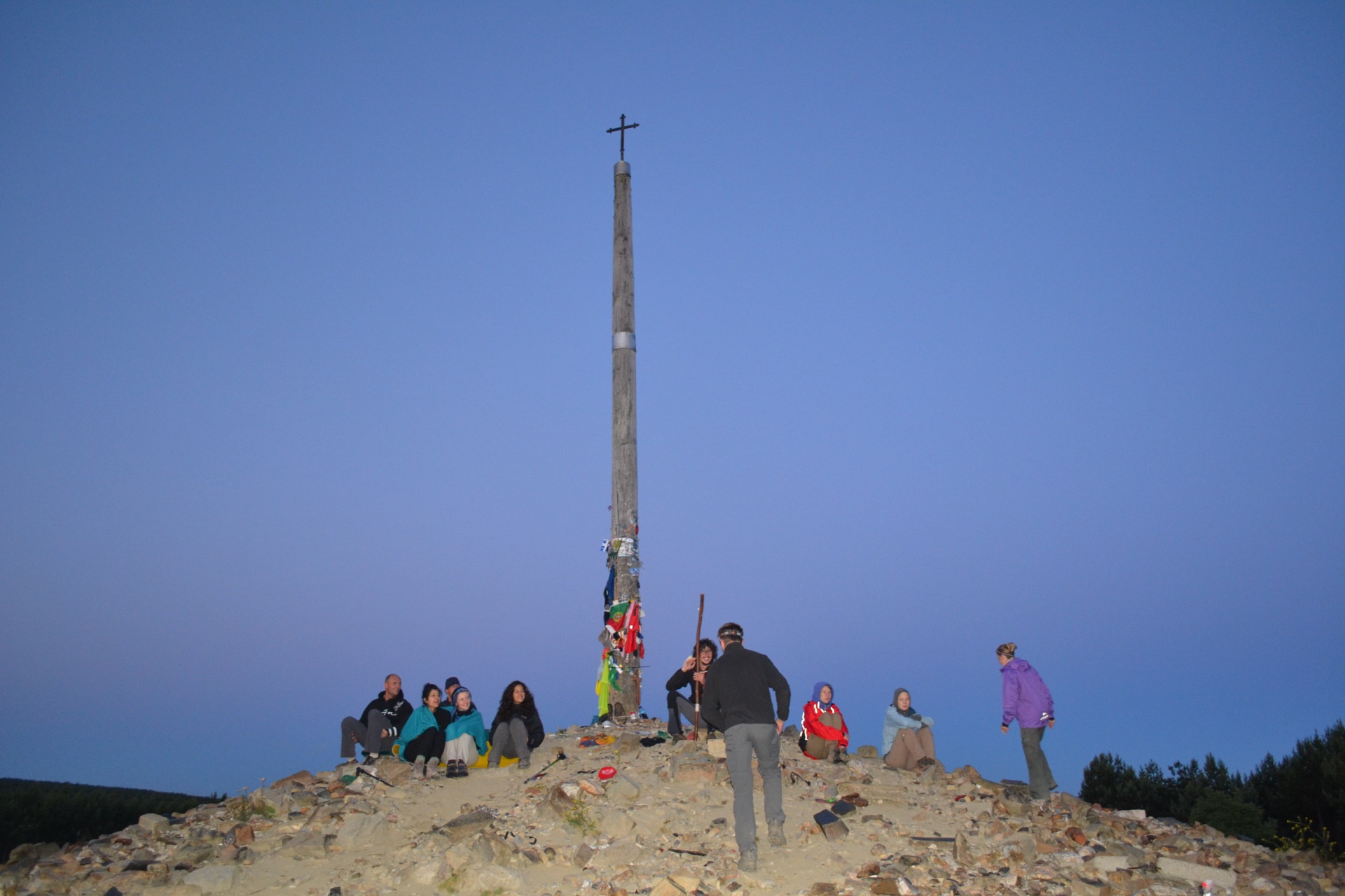 Pilgrims gathered at the foot of the iron cross under a twilight-blue sky