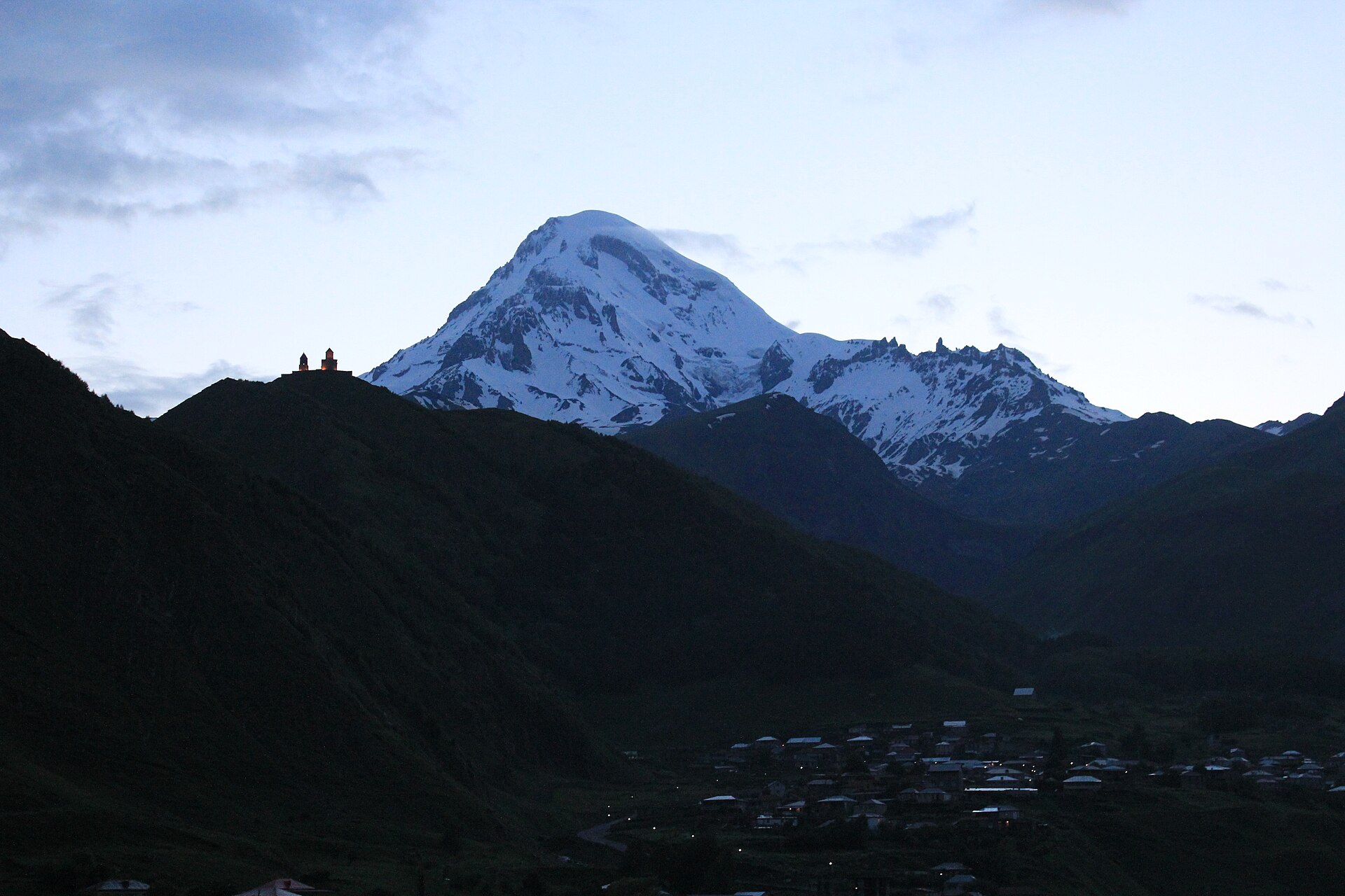 Mount Kazbek and the lit Gergeti church in blue dawn light