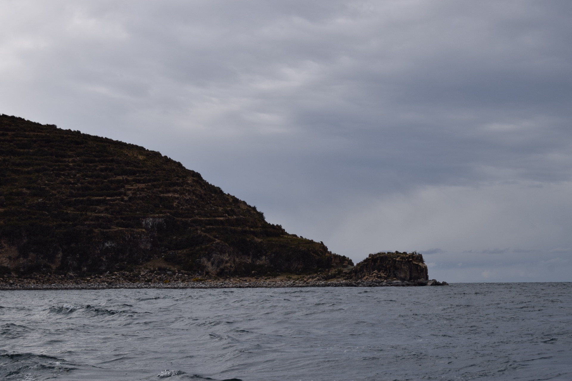 The Isla del Sol rising dark from the waters of Lake Titicaca beneath cloud
