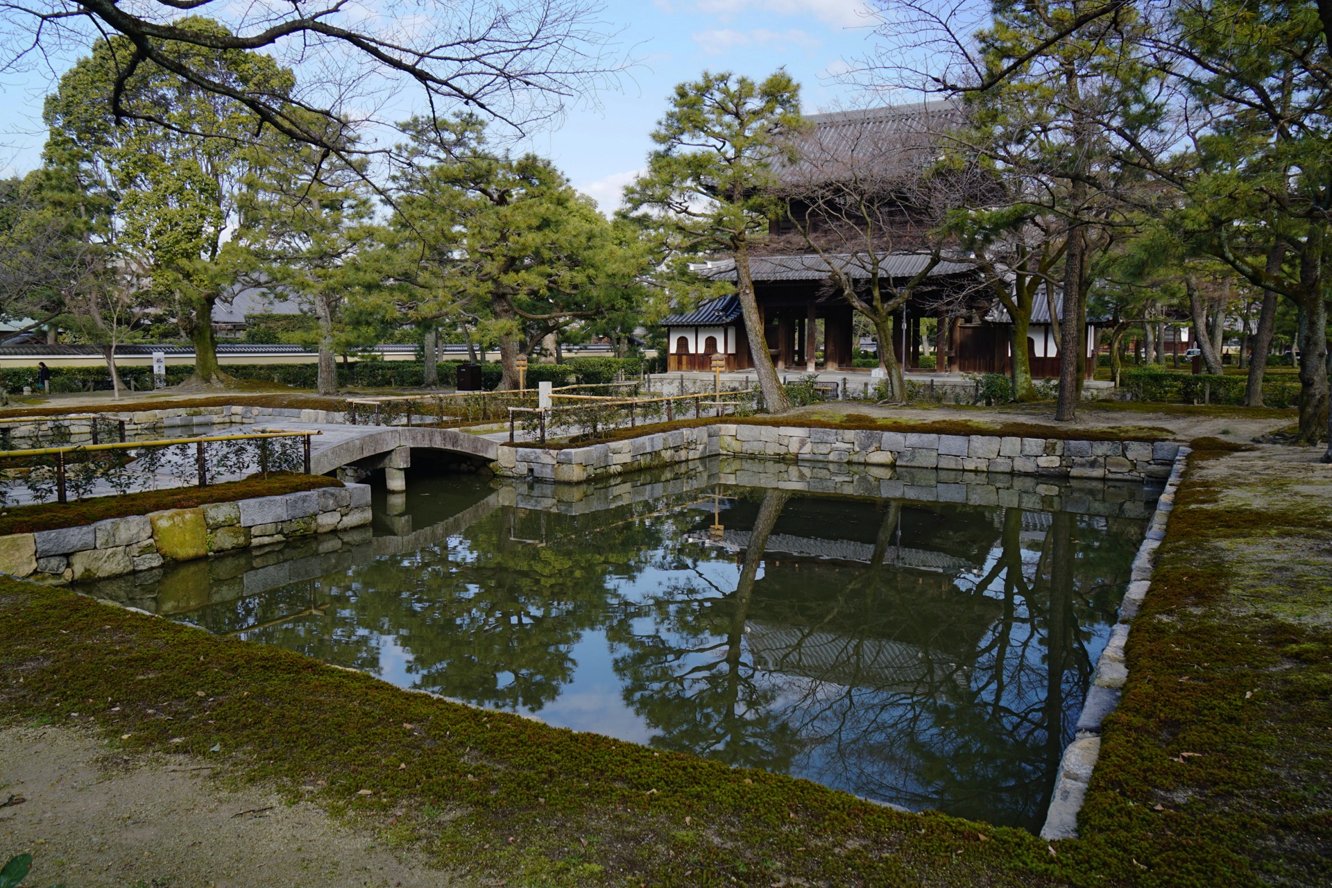 A pond and stone bridge in the grounds of Kennin-ji, the gate mirrored in the water