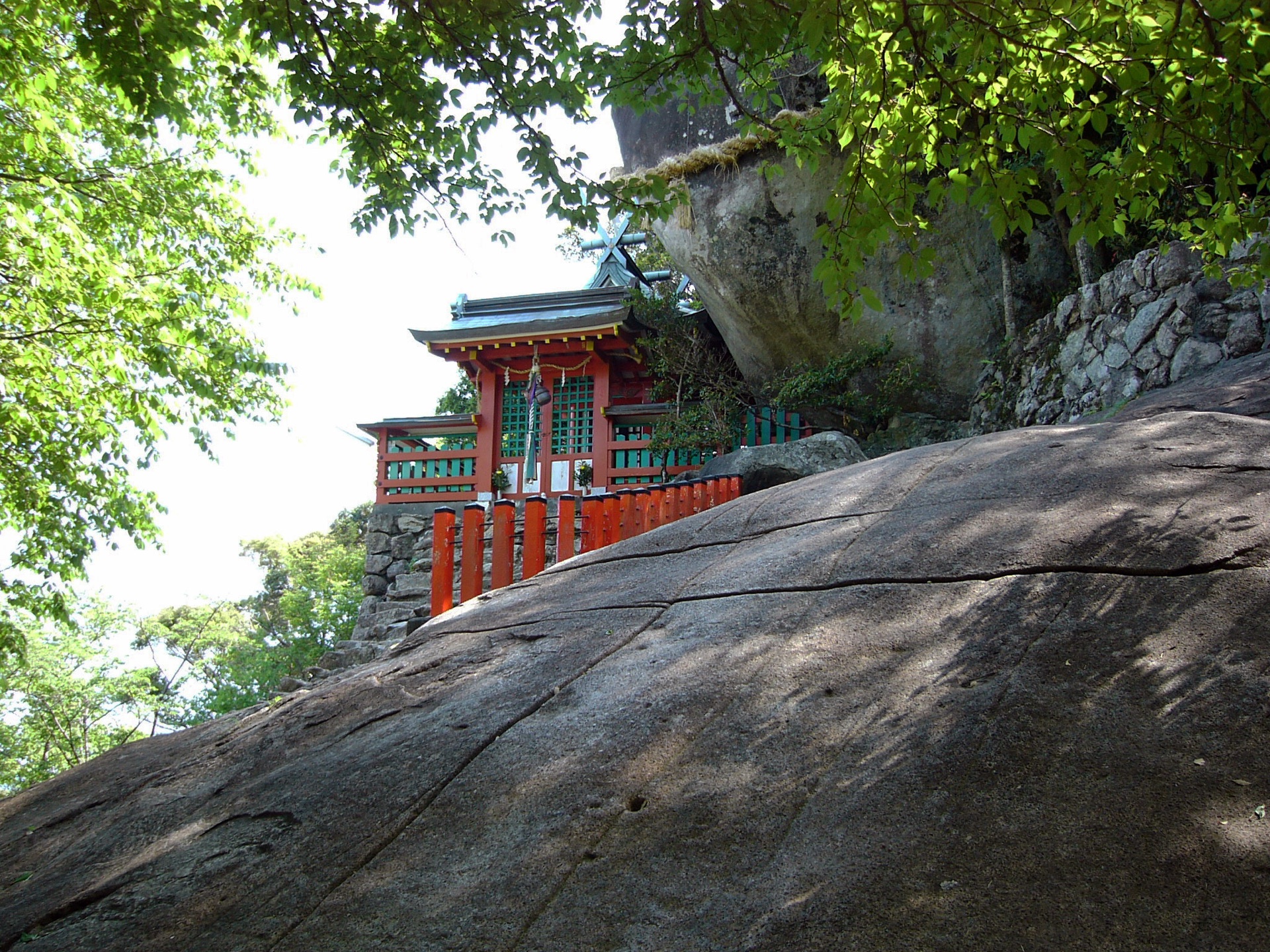 A small vermilion shrine tucked beneath a huge boulder at Kamikura Shrine