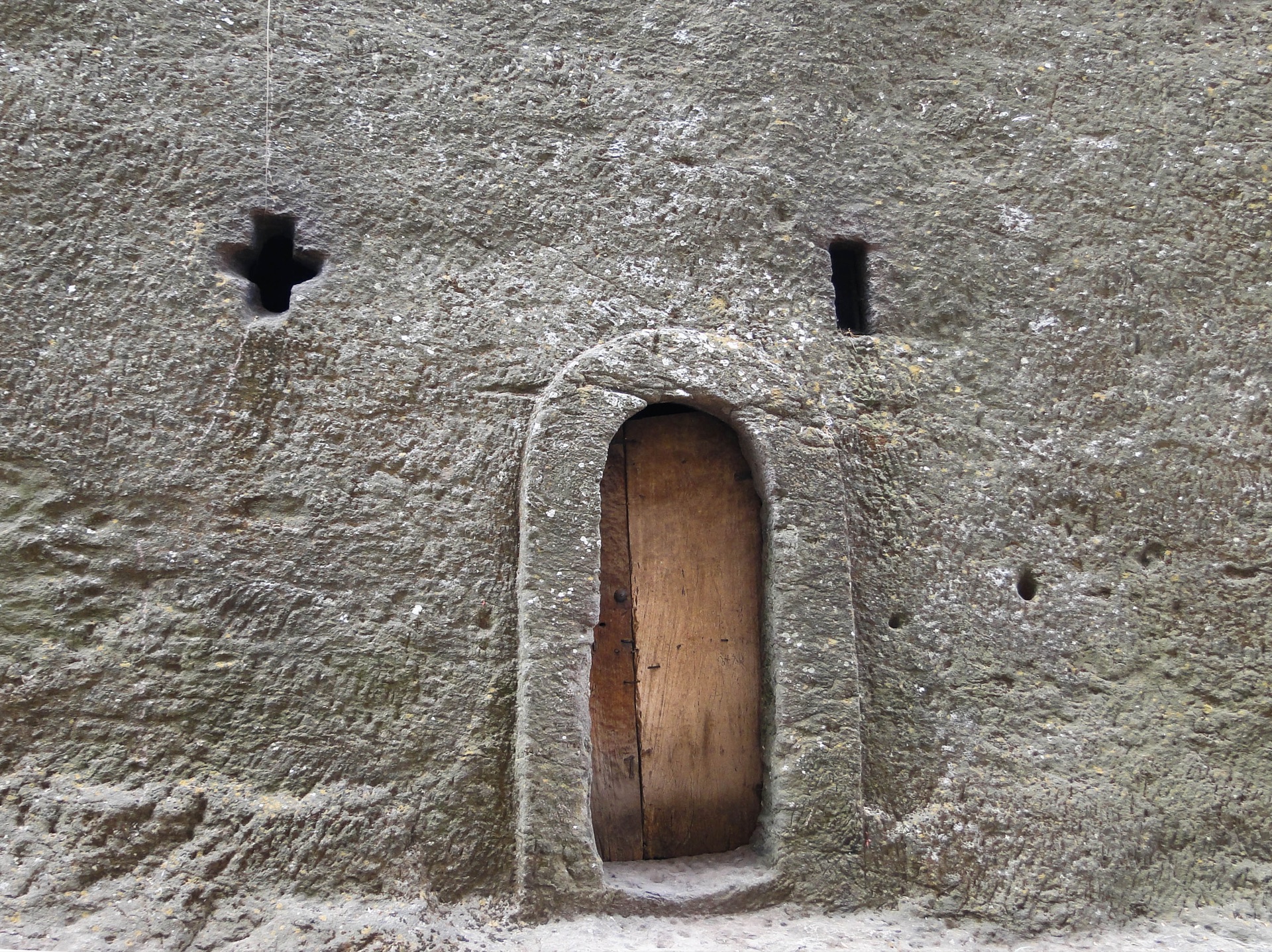 A wooden door in a wall hewn from solid rock, a cross-shaped window above