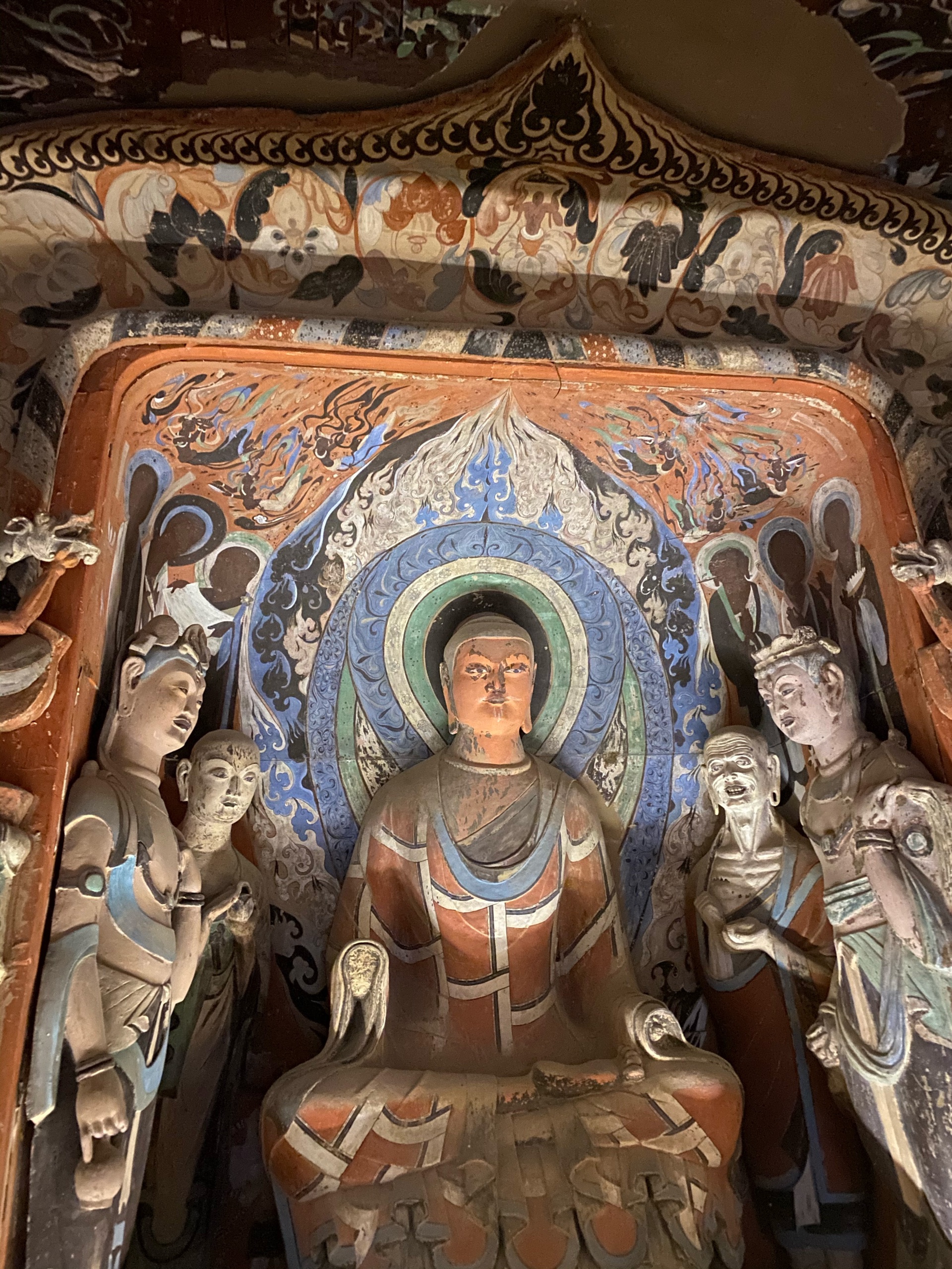 A polychrome clay Buddha with a mandorla and attendant bodhisattvas inside a Mogao cave