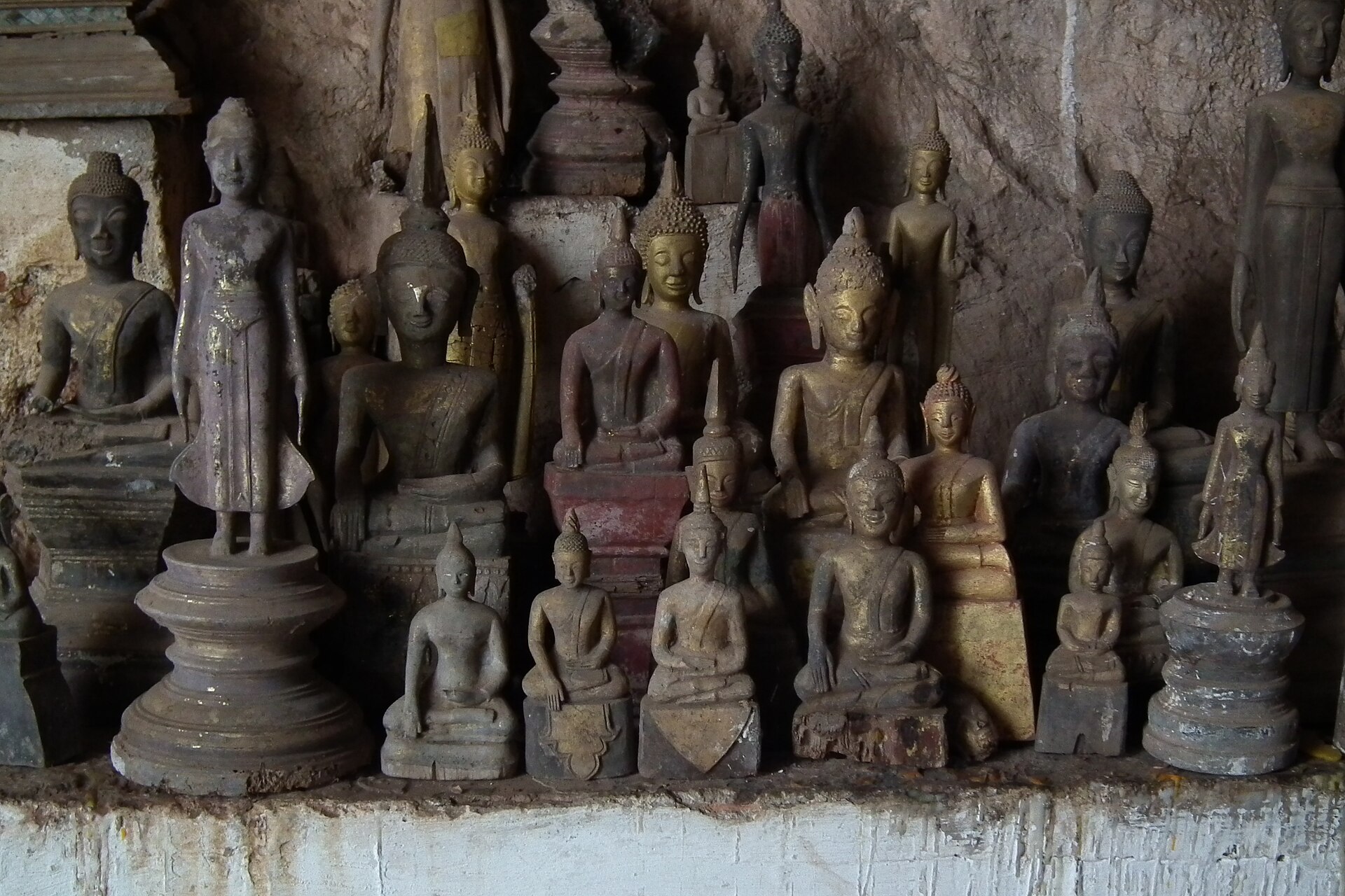 Weathered wooden Buddhas shoulder to shoulder on a shelf of the Pak Ou caves
