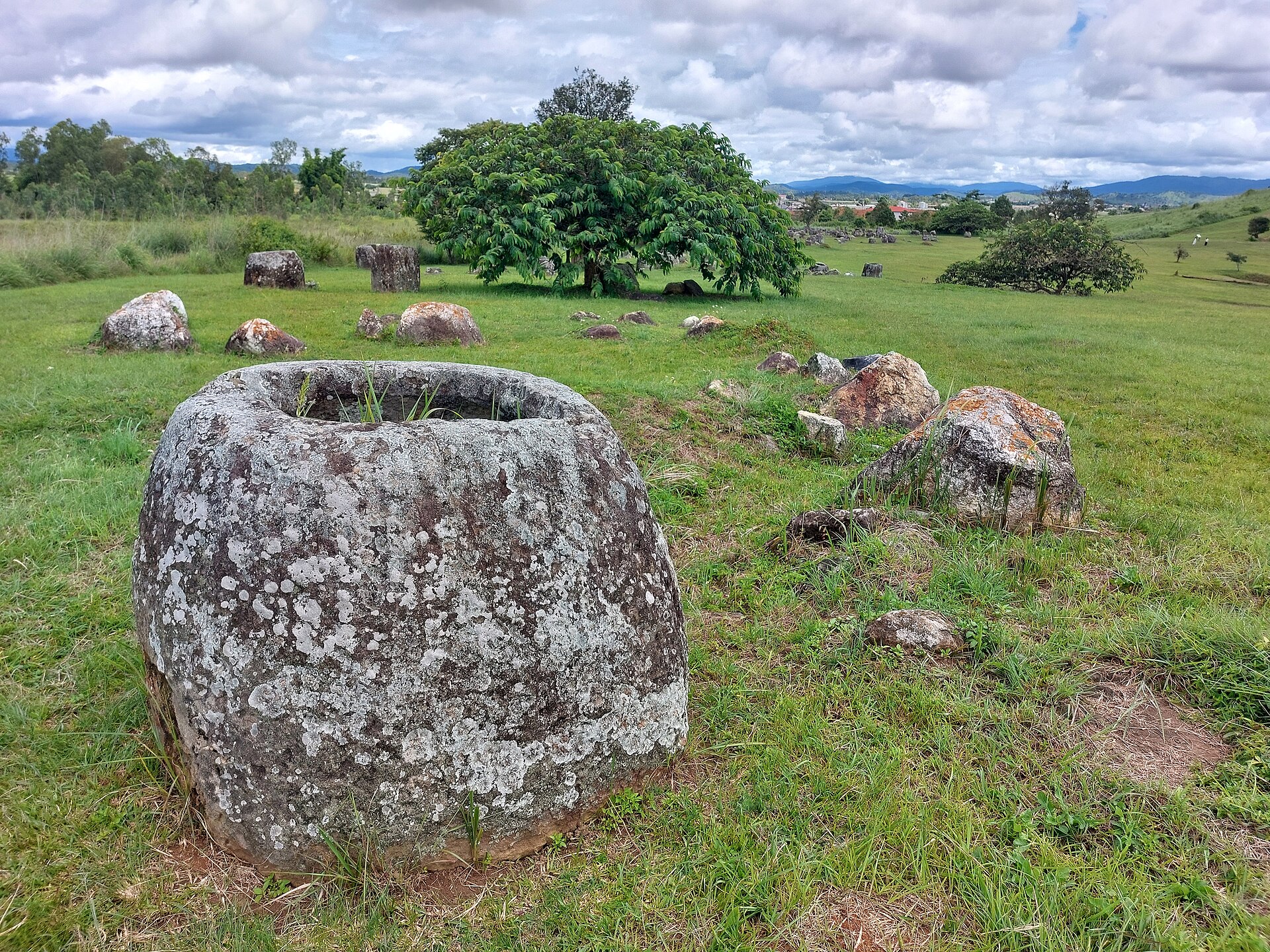 A single lichen-covered stone jar with green fields opening behind it