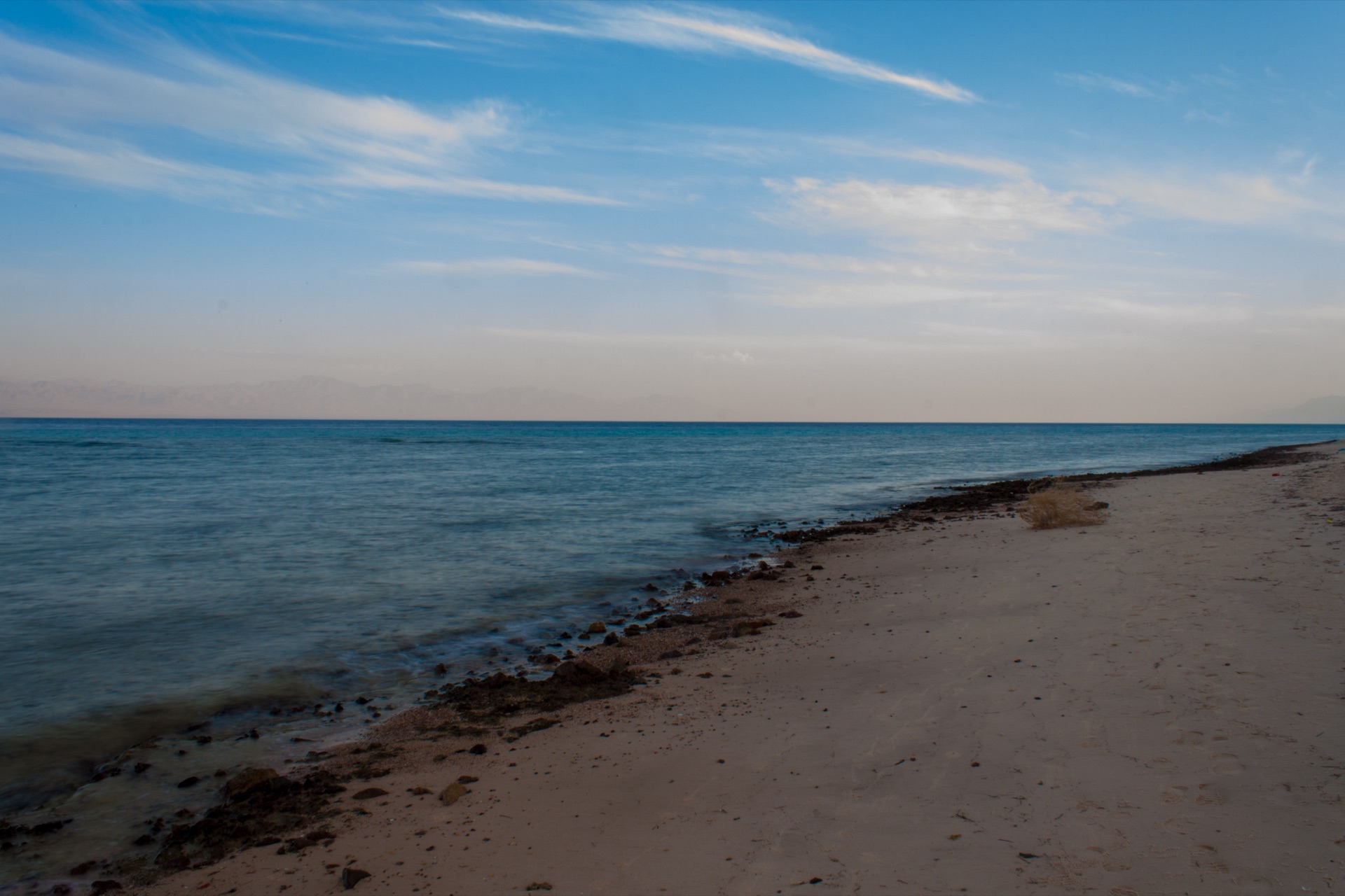 A calm, empty Red Sea shore, hazy mountains across the gulf