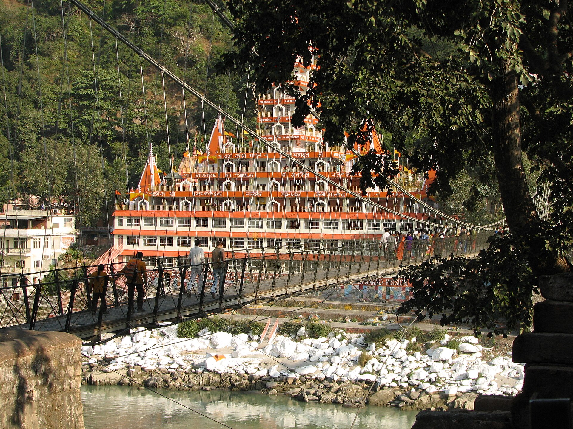 Pilgrims crossing the Lakshman Jhula footbridge, a tiered temple rising on the far bank