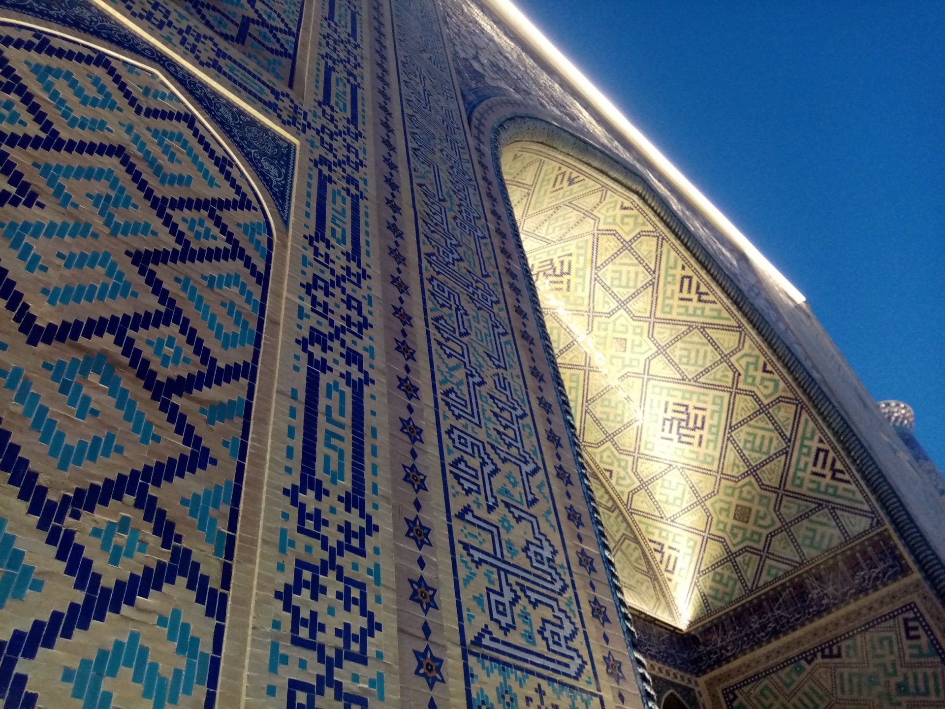 The iwan portal of a Registan madrasa in raking sunlight, its tiles patterned with stars and flowers