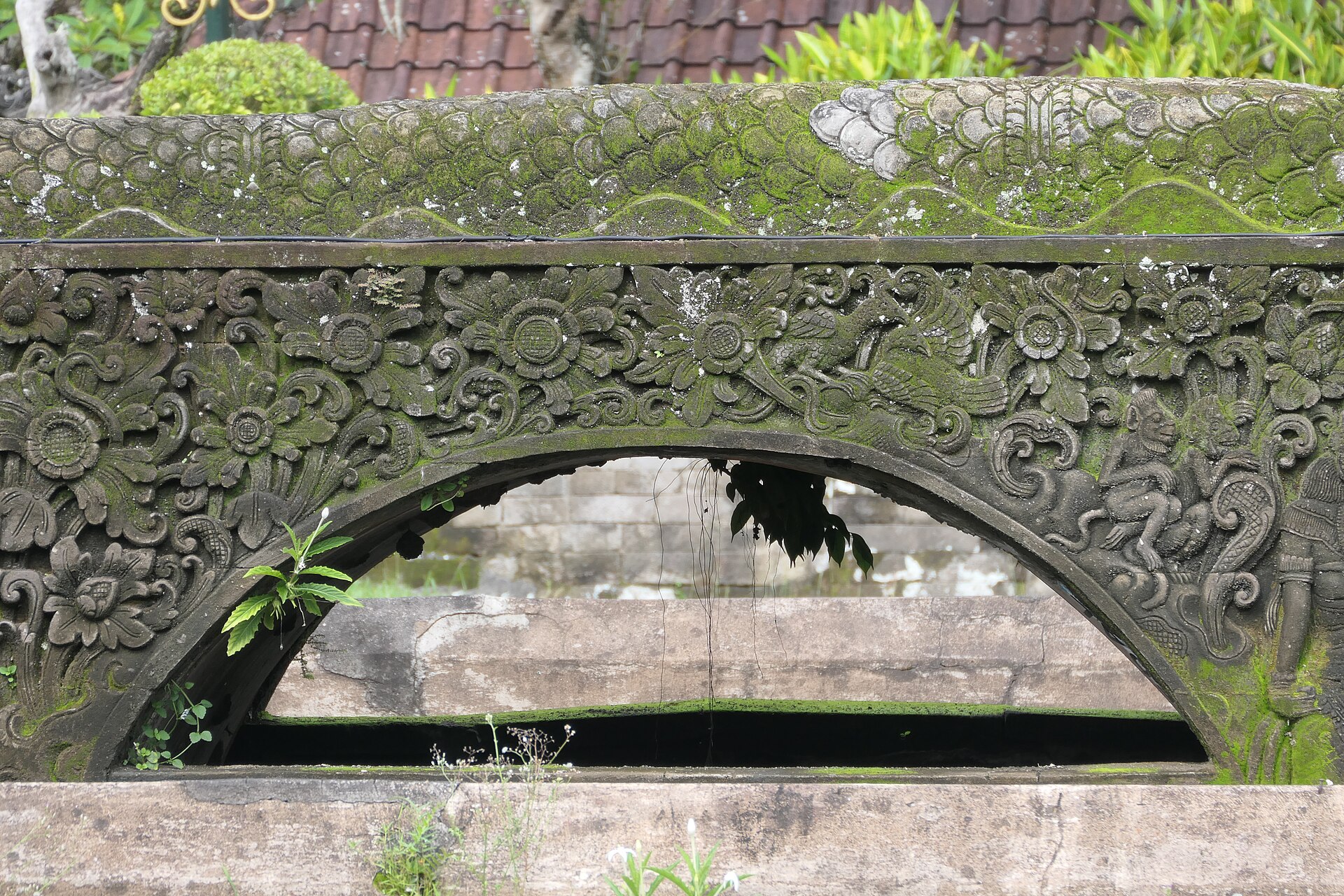 Balinese carving on the mossy stone bridge across the moat