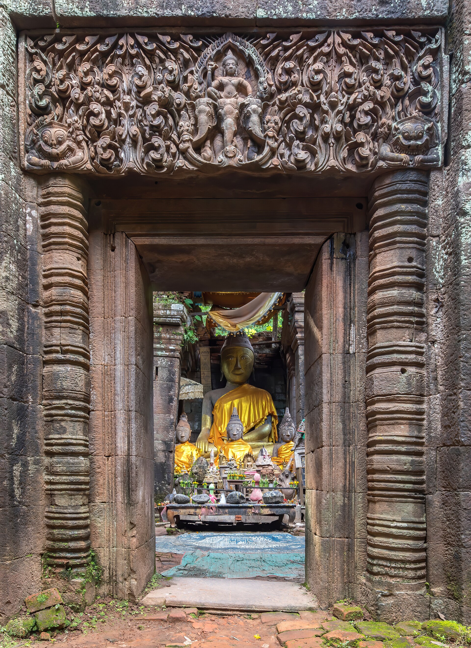 A golden Buddha seen through a Khmer stone gate carved with Indra on his elephant