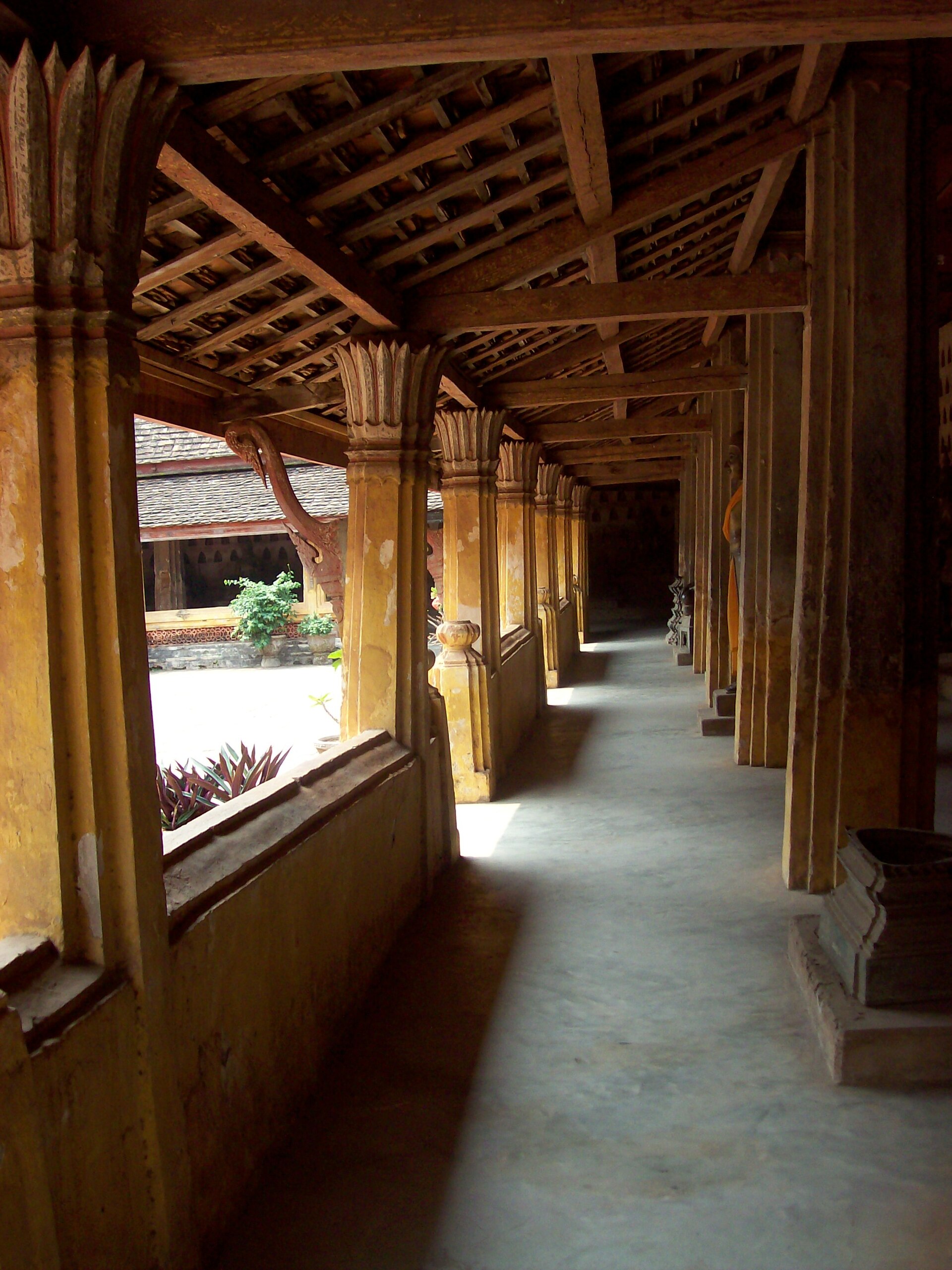 Light entering the far end of Wat Si Saket's cloister as a monk passes between yellow columns