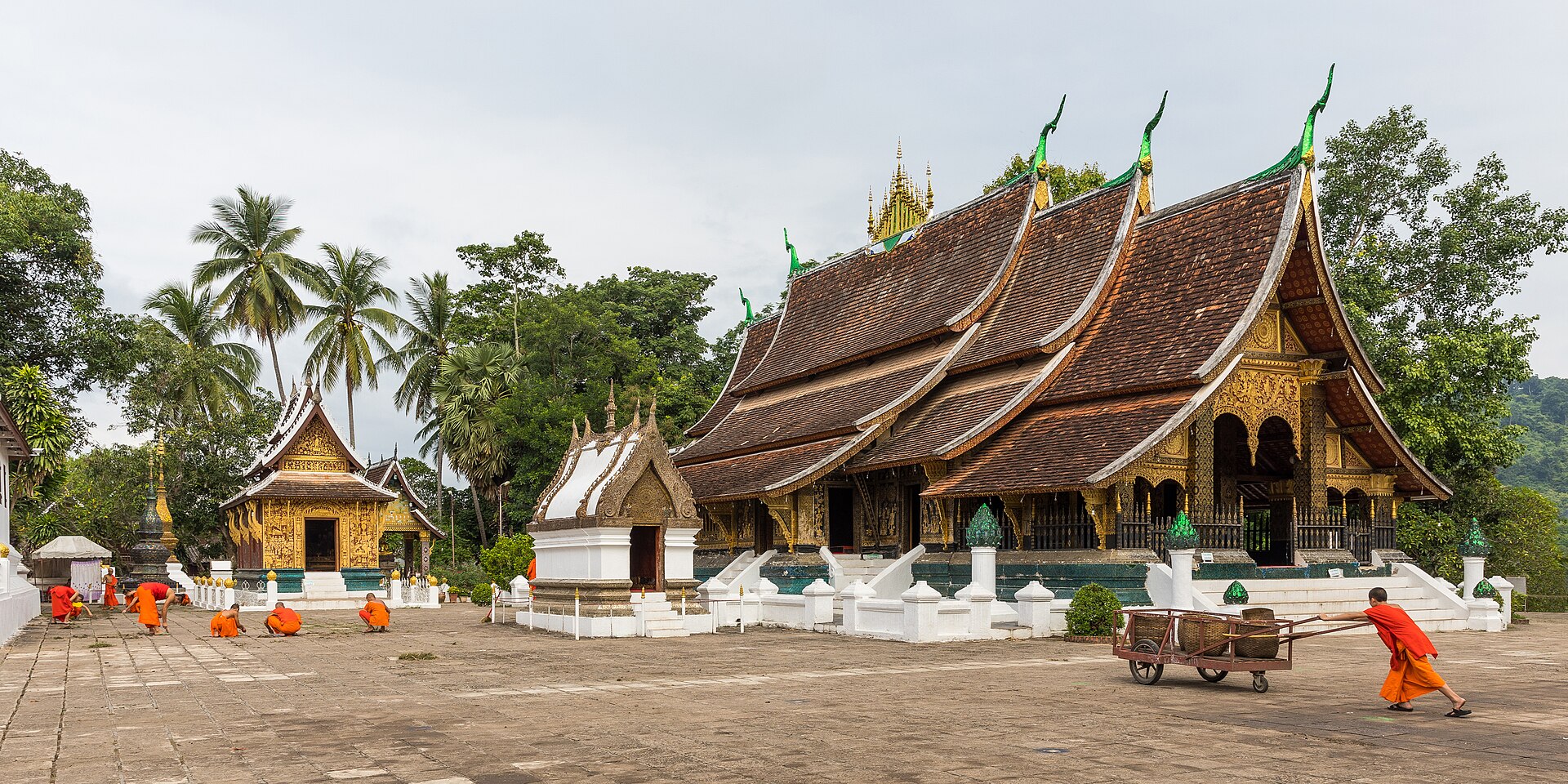 Monks in orange robes sweeping the morning courtyard of Wat Xieng Thong